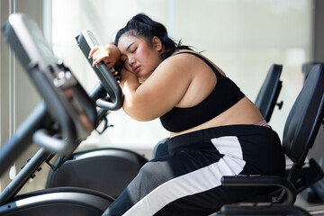 Tired fat asian woman on cycling. beautiful young chubby overweight woman wearing sporty fitness clothes doing exercise indoors at gym fitness sport club, body and health care