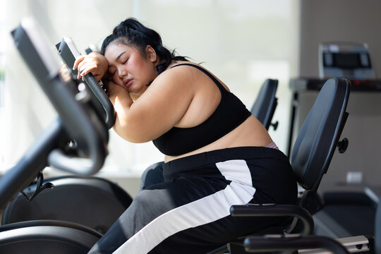 Tired fat asian woman on cycling. beautiful young chubby overweight woman wearing sporty fitness clothes doing exercise indoors at gym fitness sport club, body and health care