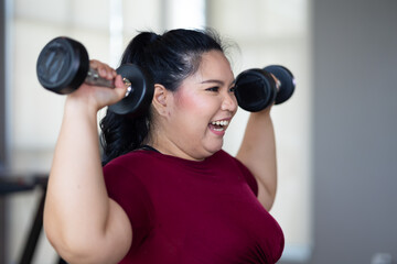 Young woman exercising with dumbbells. beautiful young chubby overweight woman wearing sporty fitness clothes doing exercise indoors at gym fitness sport club, body and health care