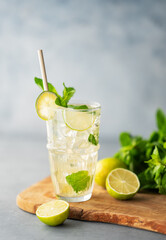 Mojito cocktail in a tall glass with lime, mint and ice on a wooden board on a blue textured background.
