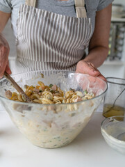 Woman is preparing a fresh pasta salad with mayonnaise, green peas, sausage and pickles in the kitchen