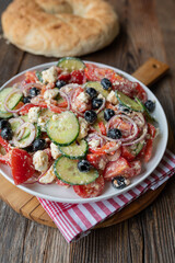 Traditional greek salad with feta cheese, peppers, black olives, cucumber, tomatoes and onions  on a plate on wooden table background. Choriátiki saláta