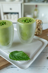 Vegetarian green pea soup fresh and homemade cooked. Served cold for delicious summer meal in glasses on kitchen counter