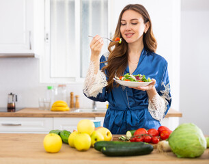 Positive housewife eating homemade salad in kitchen