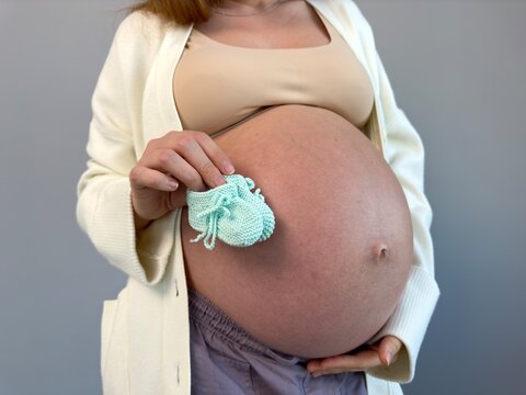 unrecognizable pregnant woman holding her future baby's booties with her big belly in the background