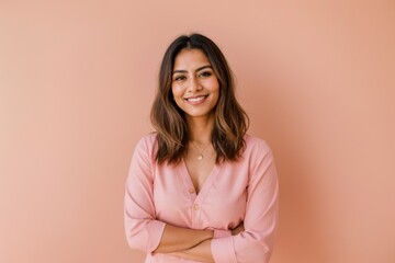 Fototapeta premium Cheerful woman with crossed arms poses against soft pink backdrop 
