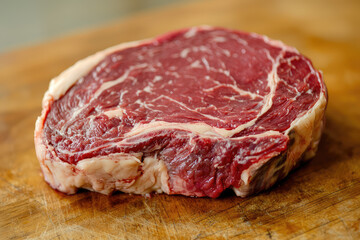 Fototapeta premium A succulent ribeye steak marbled with fat, poised invitingly on a wooden butcher block, perfect for gourmet cooking lovers.