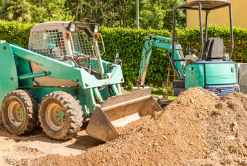 Obraz premium A worker on a Skin Loader is moving soil, excavated in front of the house. Excavation work and external paving.