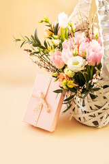 Beautiful bouquet of rose and tulips flowers and pink gift box on beige pastel background. Floral arrangement. Gift for holiday, birthday, Wedding, Mother's Day, Valentine's day, Women's Day.