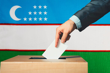 A hand holds a ballot in a ballot box against the background of the Uzbekistan flag. People throw...