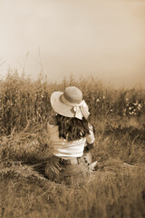 nostalgic portrait of a beautiful dark-haired woman wearing a sun hat, sitting sensuously in a cornfield, rest time, summertime, vacation