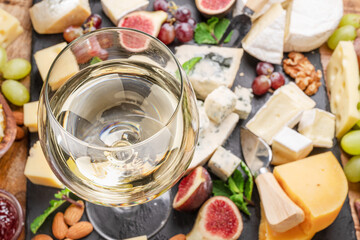 Glass of white wine with variety of sliced cheeses.