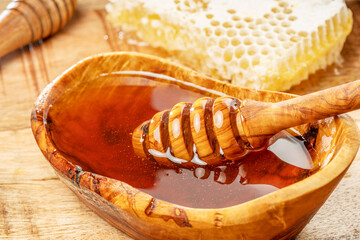 Natural organic honey in wooden bowl, honey dipper and honeycombs are near.