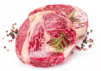 Raw beef steaks with herbs and spices ready for cooking on white background.