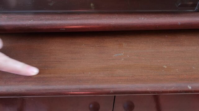 Una toma de cerca de una mano de mujer pasando el dedo por una mesa de madera llena de polvo
