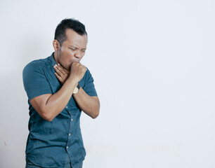 Young asian man coughing into his fist holding his throat. Isolated on white background with copyspace.