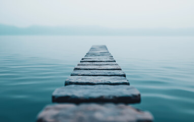 Misty morning view of a serene lake with a stone path leading into calm waters, creating a peaceful and tranquil atmosphere. Ideal for meditation and relaxation. - Powered by Adobe