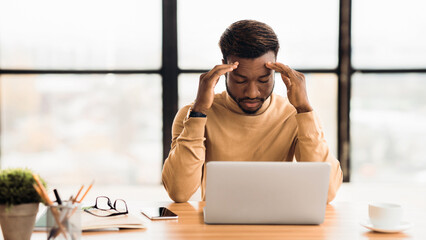 Migraine Attack. African manager suffering from headache keeping eyes closed, using laptop....