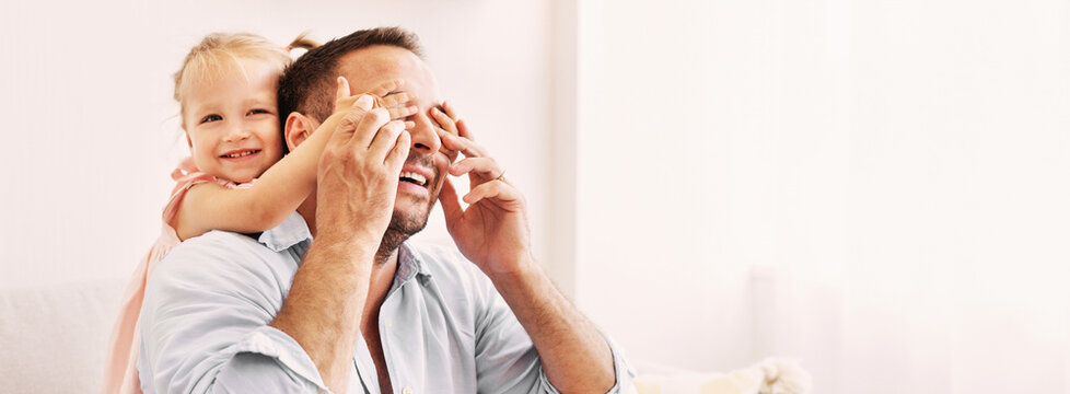 Surprise Concept. Portrait of cute blonde toddler girl covers her father's eyes and hugging from the back, copy space - Powered by Adobe