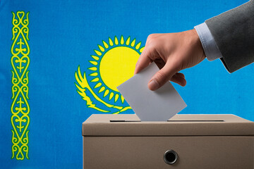 A hand holds a ballot in a ballot box against the background of the flag of Kazakhstan. People...