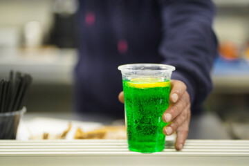 A bartender pass a plastic cup with a summer refreshing cocktail in green color made of mint with alcohol and fresh lemon