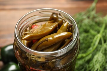 Tasty pickled jalapeno peppers in jar on table, closeup