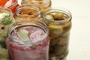 Different pickled products in jars on light table, closeup