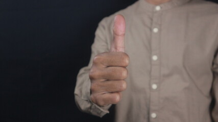 Business man in brown shirt gives thumbs up isolated on black background