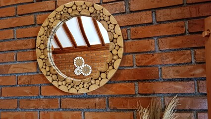 A round mirror with wooden frames is hanging on a brick wall