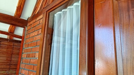 A window with a white curtain is shown in a wooden frame