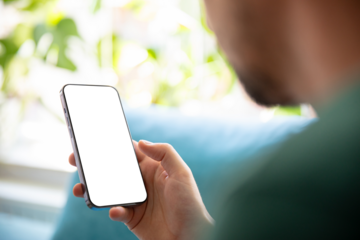 Person holding a smartphone with a blank screen, relaxing on a sofa in a bright, green environment. Perfect image for presenting mobile apps, user interfaces, or design templates.