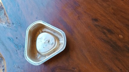 A small, dirty, and rusted tin is sitting on a wooden table
