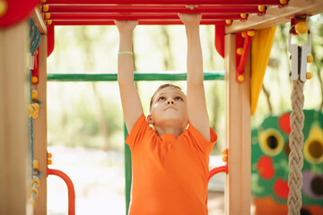 Fototapeta premium Kid teenager boy doing pull ups on horizontal bar. Active kid exercising and doing pull ups on metal sports equipment.
