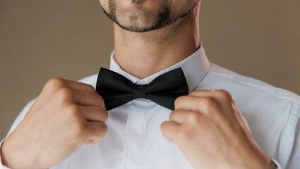 Groom adjusting his black bow tie, symbolizing elegance and style on his wedding day