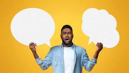 Complex choice. Confused black guy holding two speech bubbles on yellow background, panorama