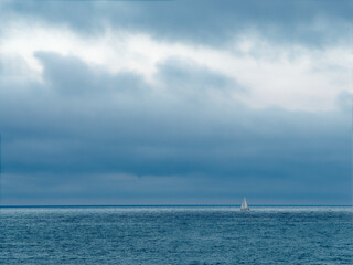 Obraz premium Calm sea with a distant sailboat under dark contrasted clouds, copy space, Palavas-les-Flots, France