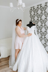 Fototapeta premium A woman is standing in front of a wedding dress. She is wearing a pink gown and a tiara