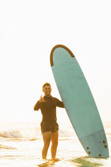 Happy surfer making hand gestures next to his surfboard