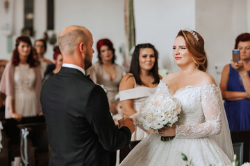 Naklejka premium A bride and groom are getting married in a church. The bride is wearing a white dress and the groom is wearing a suit. The bride is holding a bouquet of flowers and the groom is holding her hand