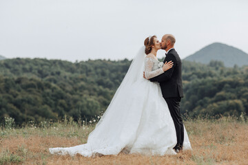 A bride and groom kiss in a field. The bride is wearing a long white dress and the groom is wearing a black suit. The scene is peaceful and romantic