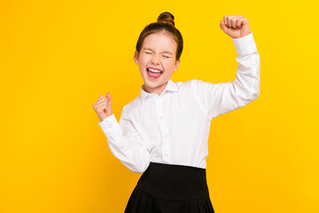 Photo of cute schoolgirl raise fists empty space wear uniform isolated on yellow color background