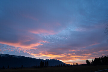 A breathtaking canvas of pink hues paints the sky as the sun dips below the horizon. Soft, wispy clouds drift across the sky, bathed in a warm, rosy glow. 