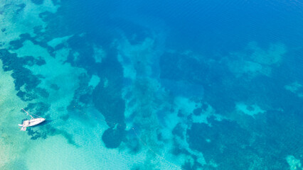 Fototapeta premium Aerial top-down view of a sailboat anchored in a turquoise bay on the beautiful Greece shore. Yacht on the water surface from top view. Summer seascape from air. Travel concept and idea