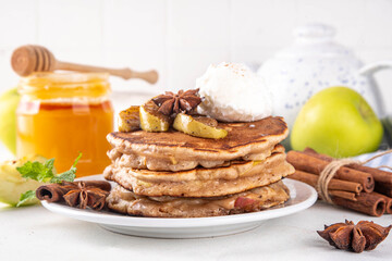 Sweet autumn apple pie pancakes stack with ice cream and caramelized apples on top, won kitchen table with spices, apples and honey jar, copy space