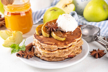 Sweet autumn apple pie pancakes stack with ice cream and caramelized apples on top, won kitchen table with spices, apples and honey jar, copy space