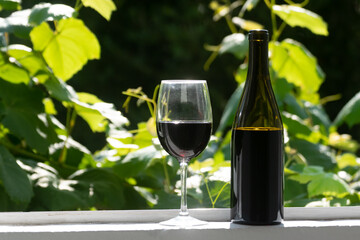 Glass and bottle of red wine on window sill with vine leaves in background