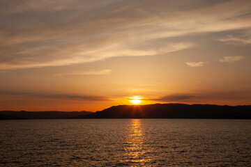 Sun going down on the horizon with red clouds over a mountain and lake