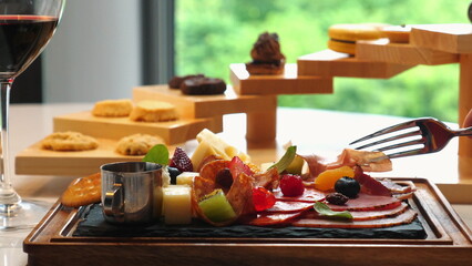 Elegant charcuterie board with assorted fruits, cheese, and cured meats in fine dining restaurant, accompanied by glass of red wine and gourmet desserts in background. Fine Dining and Culinary Art.