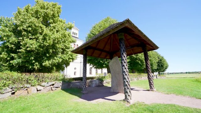 The iconic Rokstenen, a Viking Age runestone, stands proudly in its protective shelter surrounded by lush greenery in odeshog, Sweden.