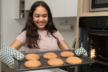 Young girl proudly holding tray of freshly baked cookies in kitchen